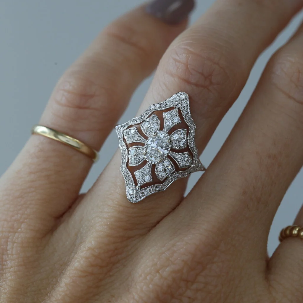 Art deco style milgrain platinum engagement ring with oval center diamond.